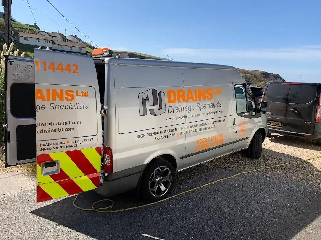 MJ Drains silver van parked in Devon, showing company branding and listed drainage services.