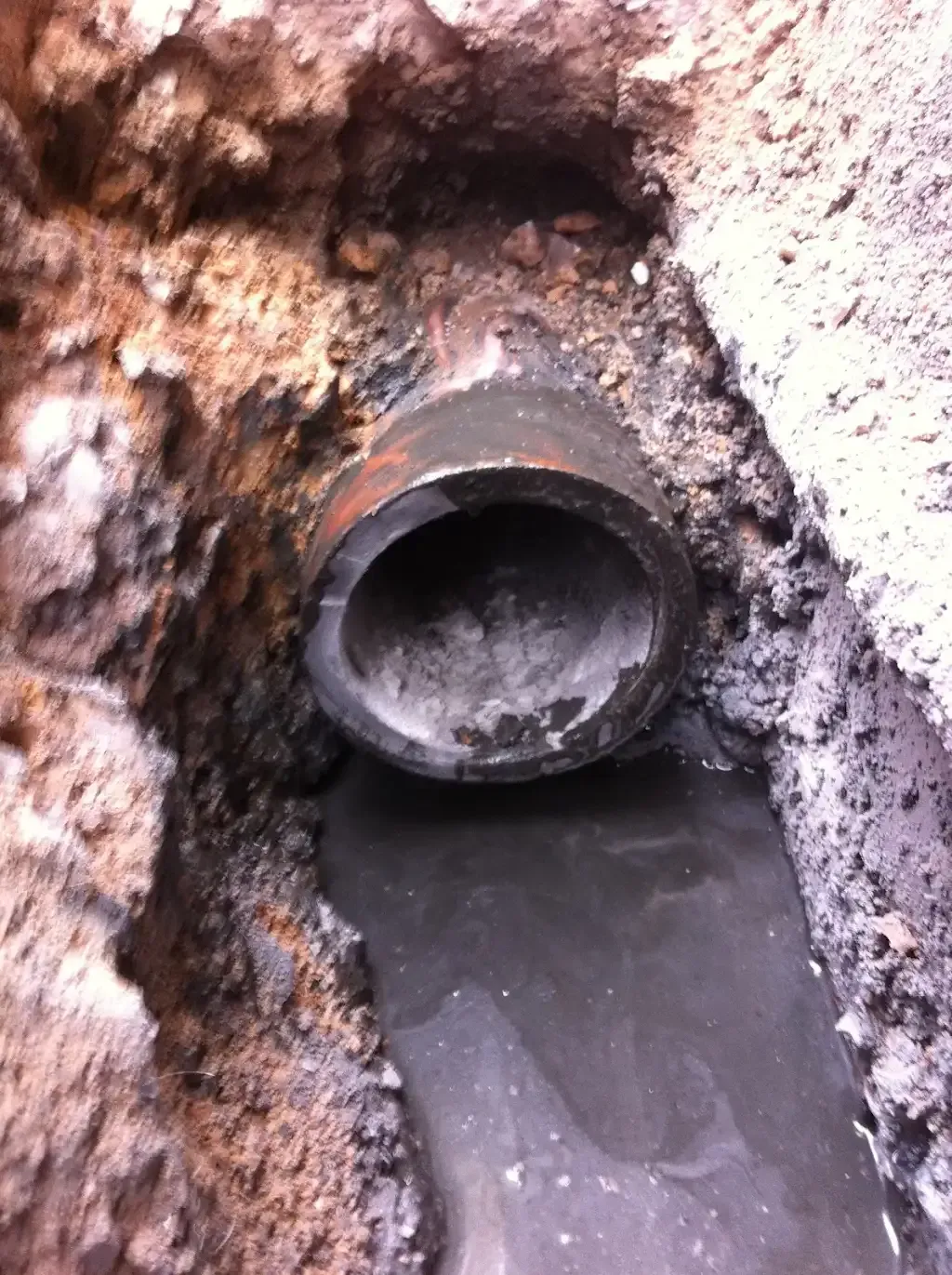 Exposed drain pipe in excavated ground with water accumulation.