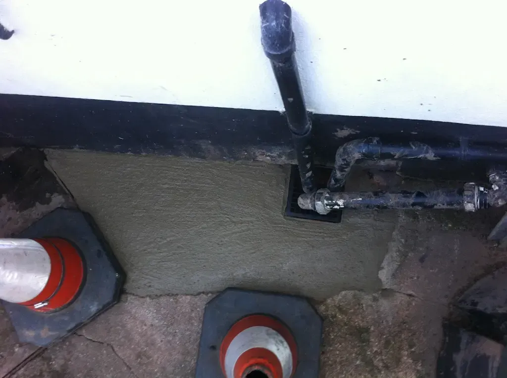 Newly laid concrete covering drainage pipes and a grate after access work, with traffic cones nearby.