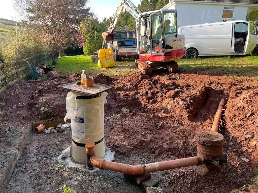 Foundation drainage work in progress with excavation, new drainage pipes, an inspection chamber, and an excavator on site.