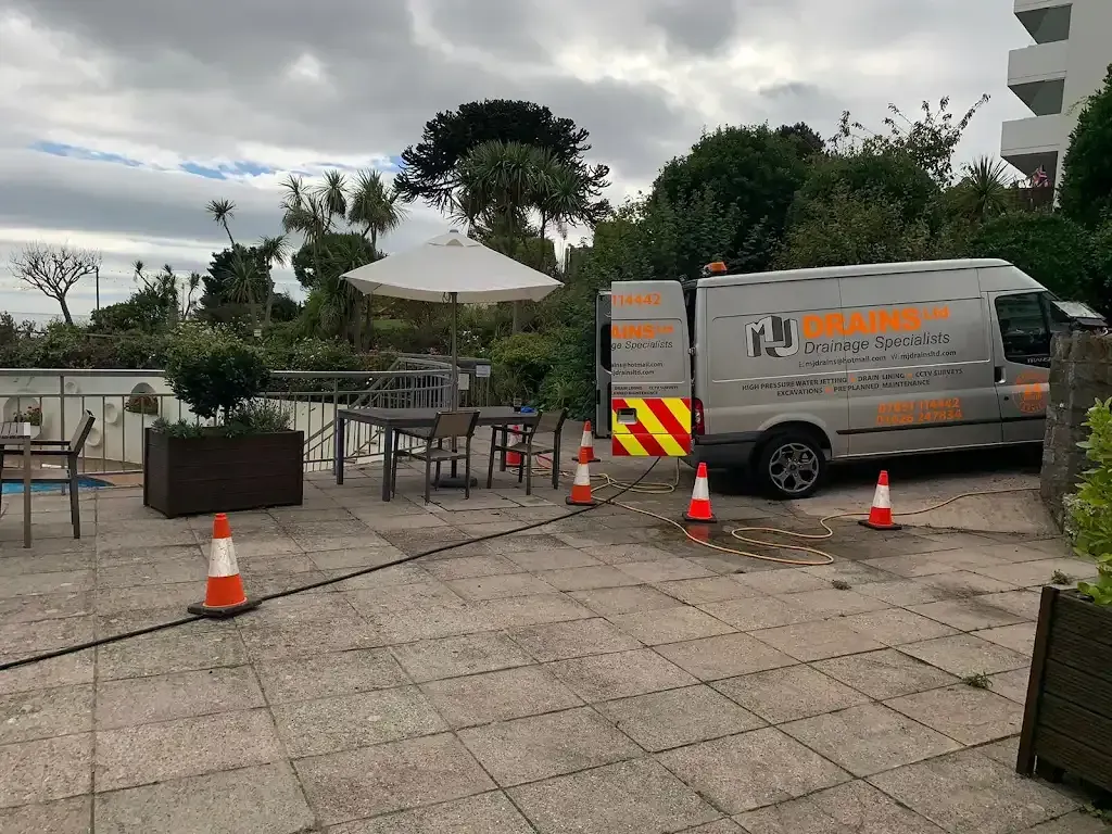 MJ Drains van with hoses and safety cones set up on a patio for drainage service, possibly near a pool.